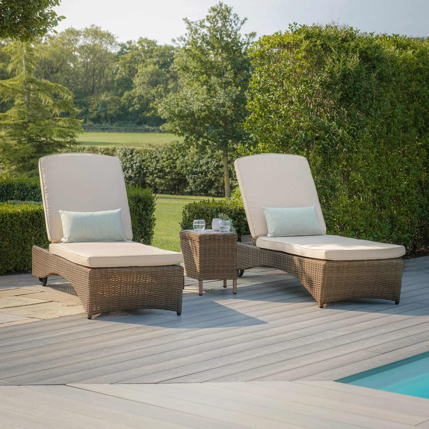 Rattan sun lounger set with cream cushions and glass table beside pool on patio