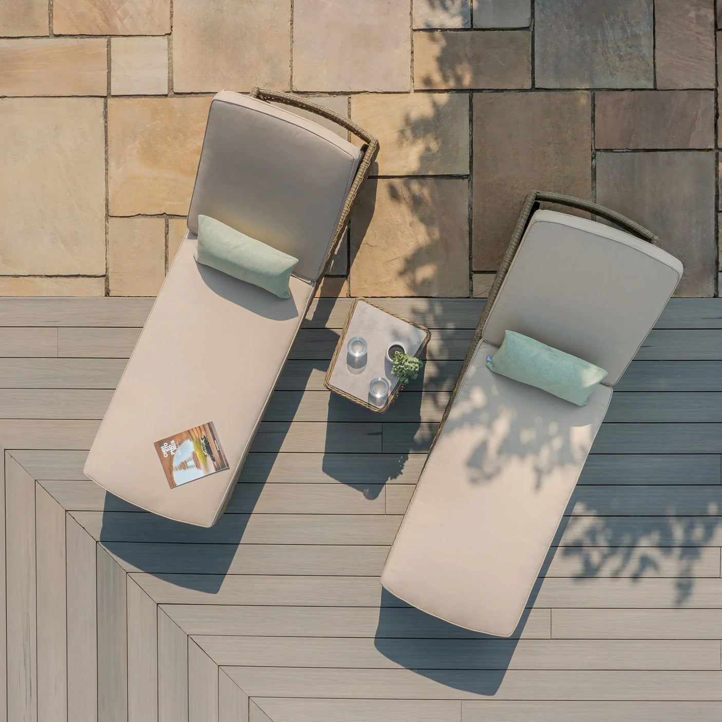 Beige outdoor sun loungers with green cushions on a patio beside a small side table