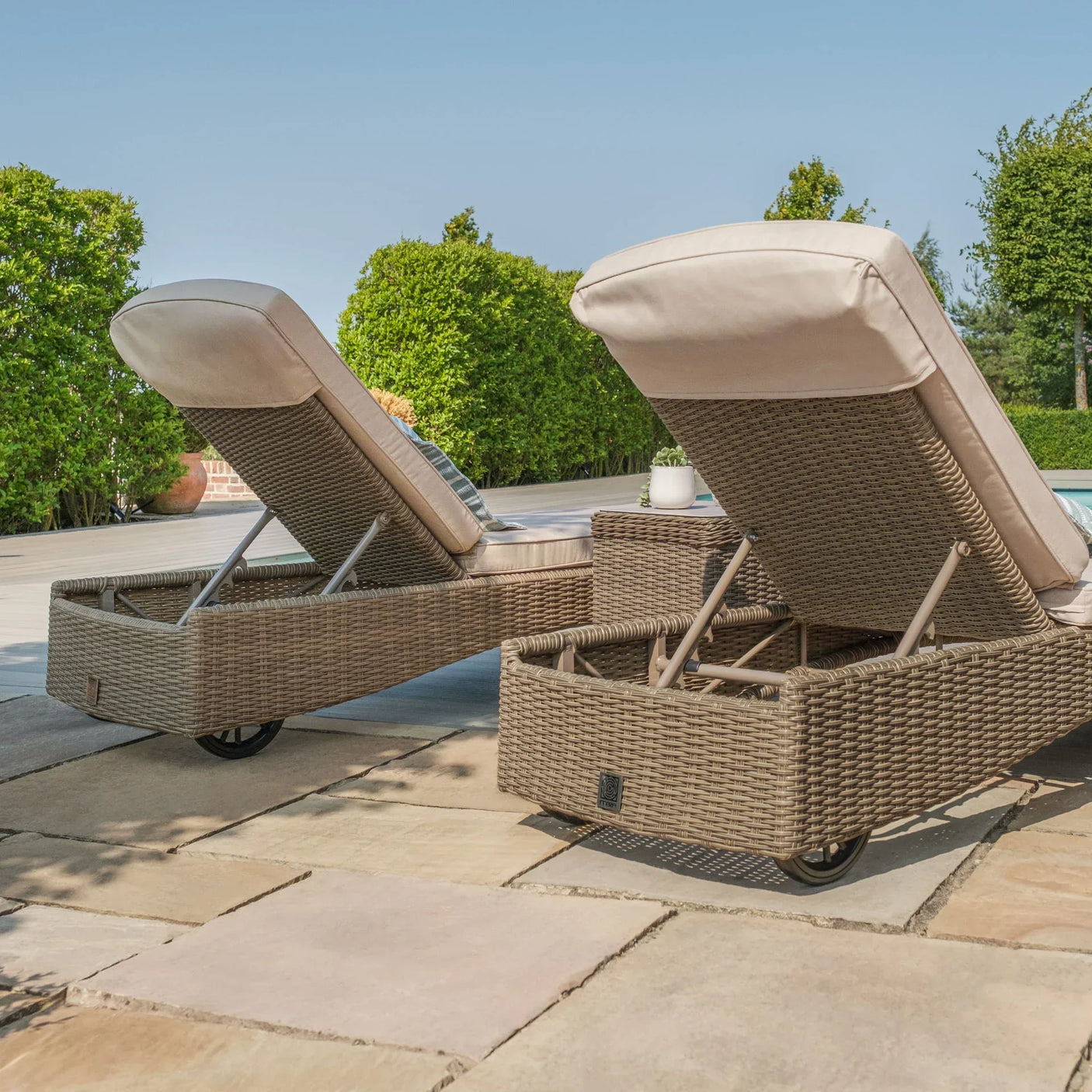 Rattan sun loungers with beige cushions on patio beside pool and garden