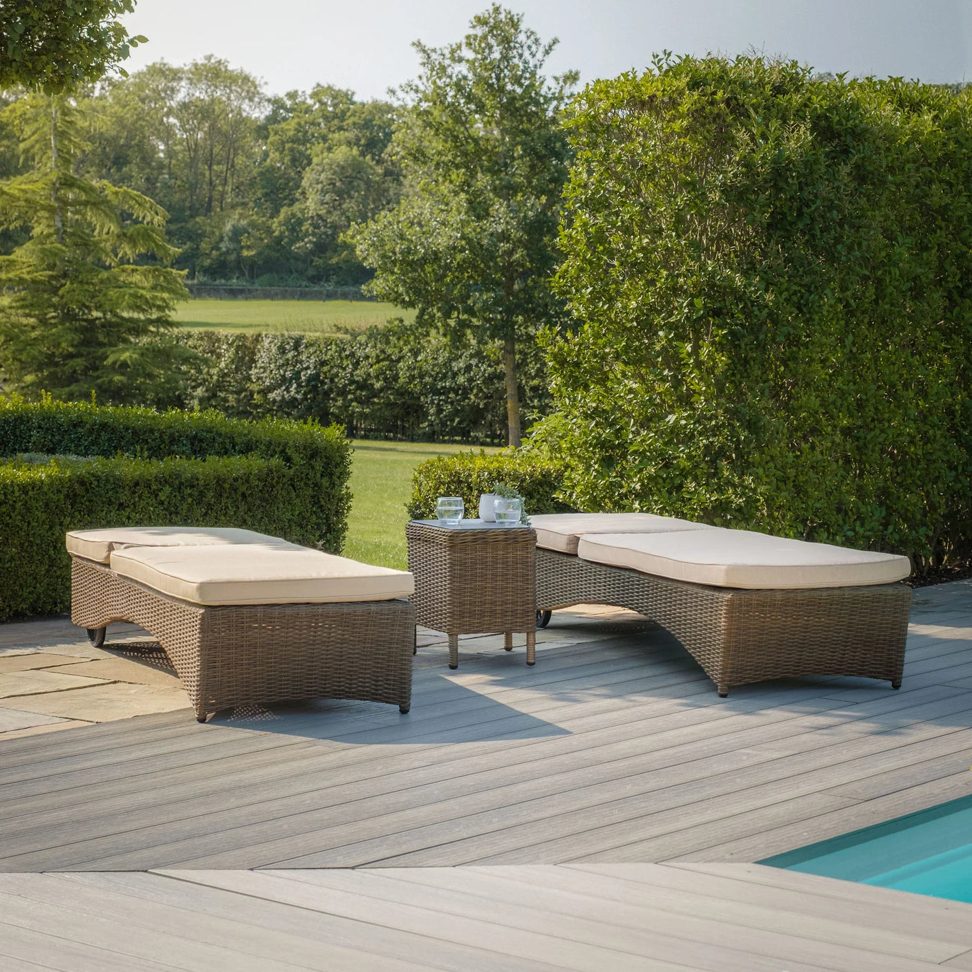 Rattan outdoor sun loungers with cream cushions and matching side table by a pool