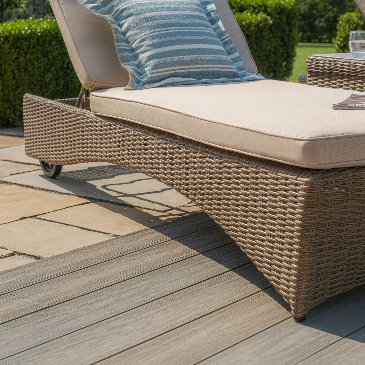 Rattan garden sun lounger with beige cushion and a striped pillow on patio