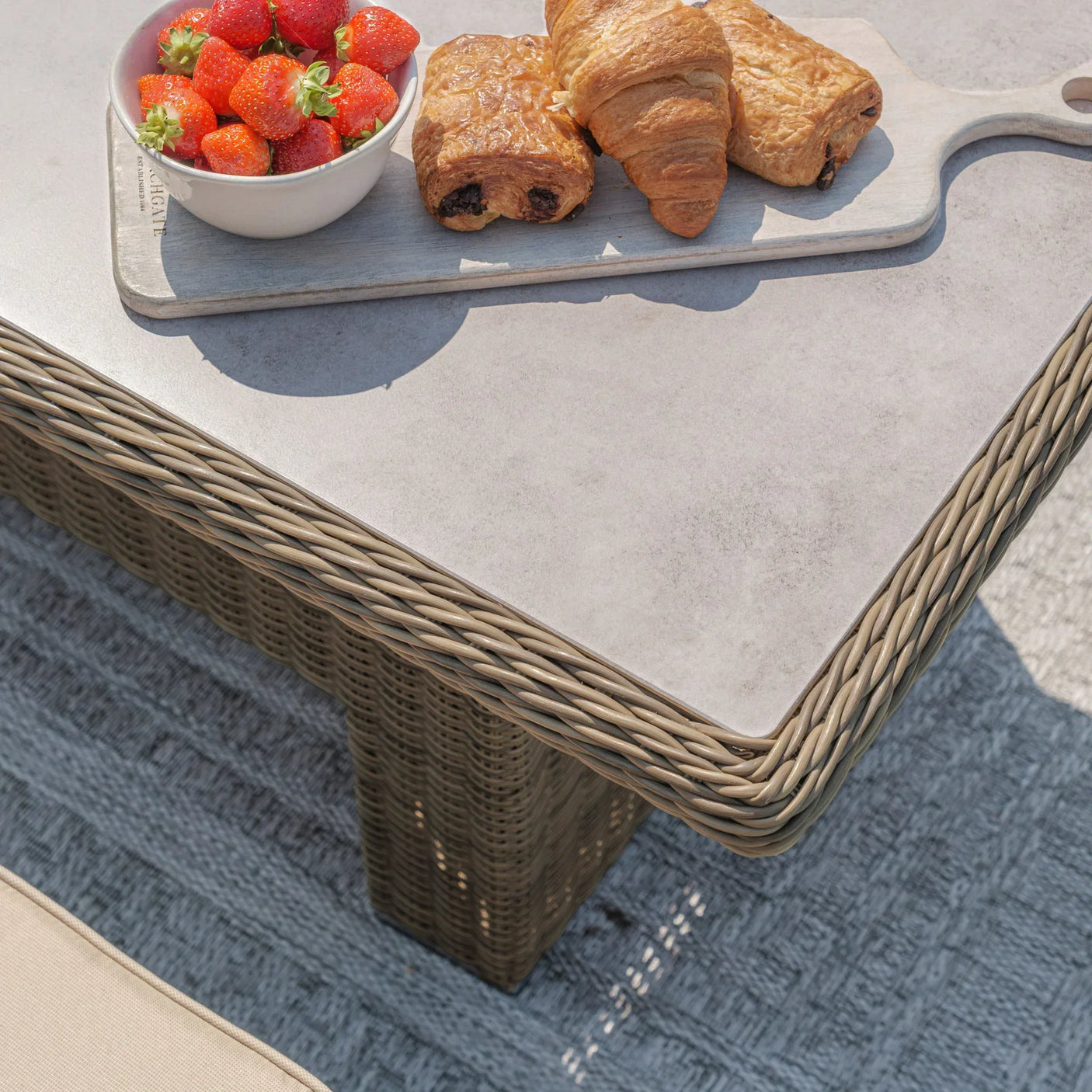 Rattan garden table with grey top, pastries and strawberries on serving board