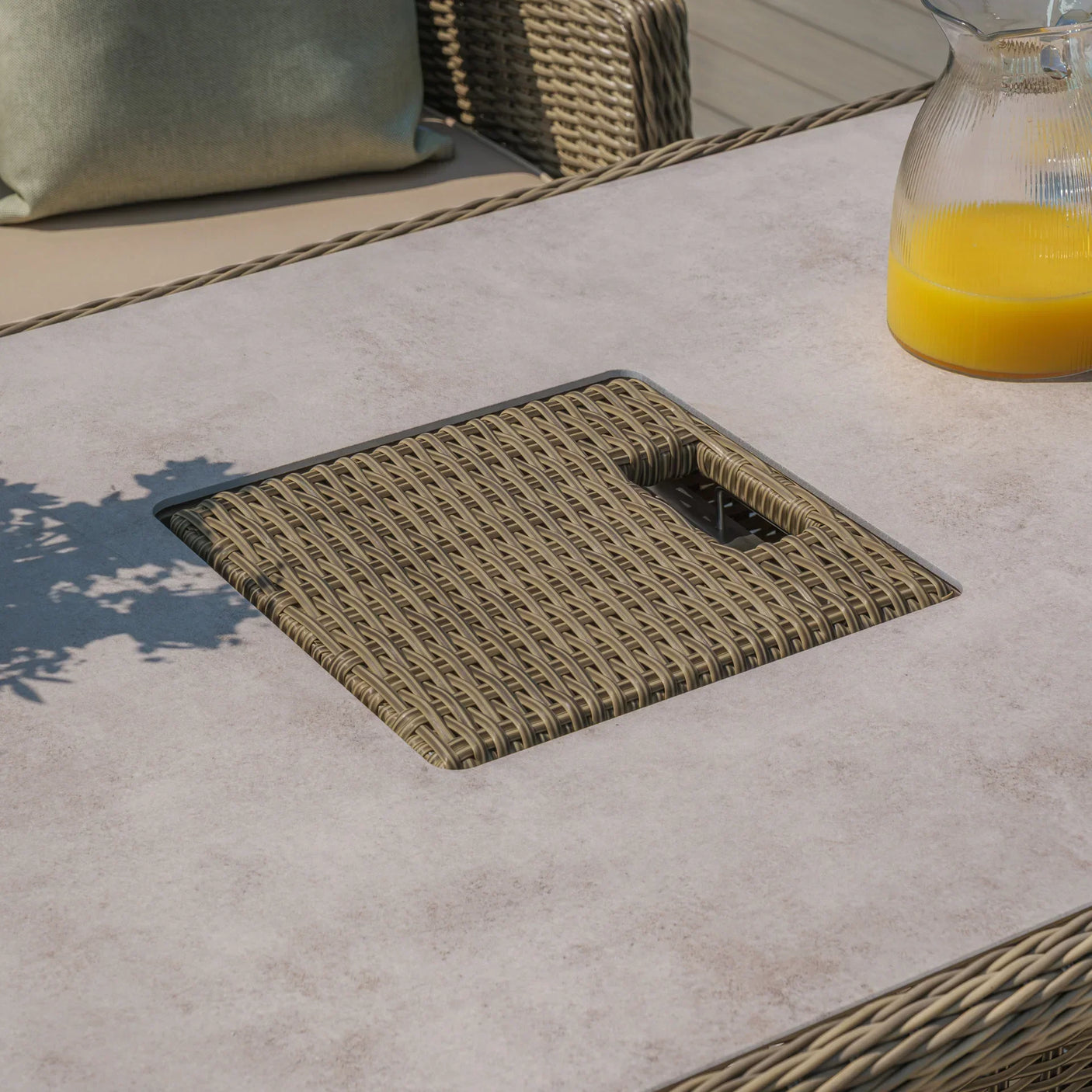 Rattan outdoor dining table with square fire pit lid and glass jug of orange juice