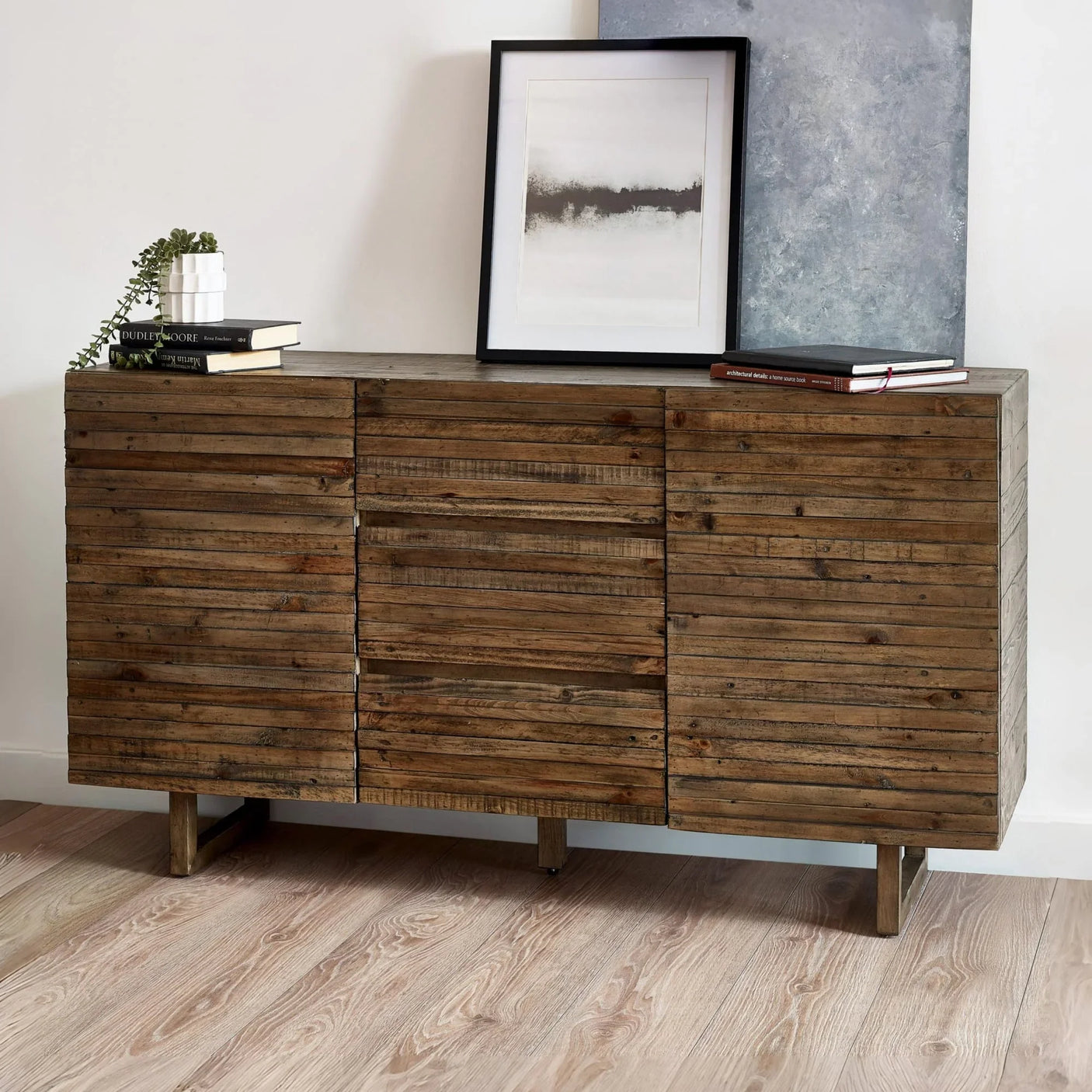 Rustic wooden sideboard with textured slatted doors, books, and framed art on top