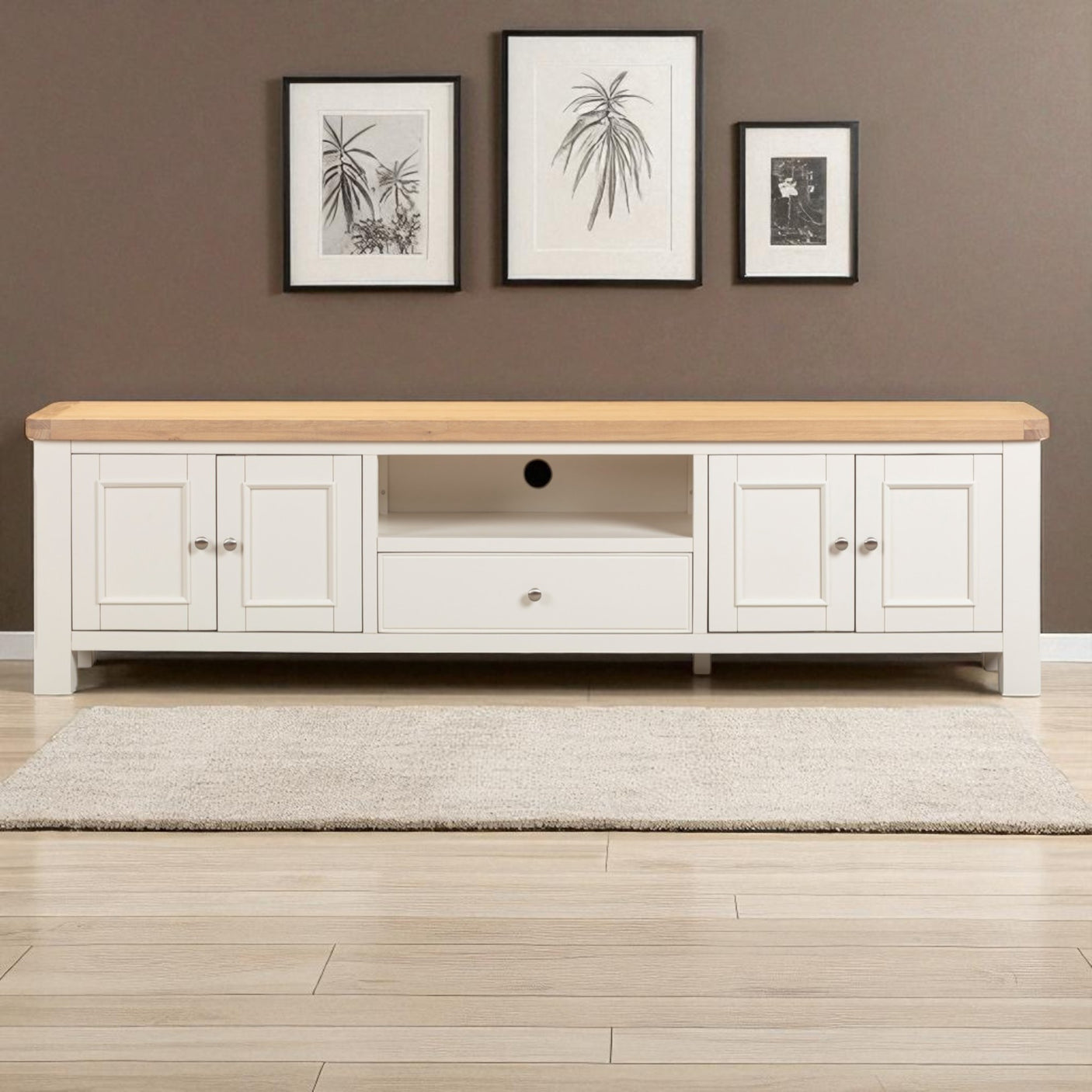 White entertainment console with wooden top against a brown wall with framed pictures.