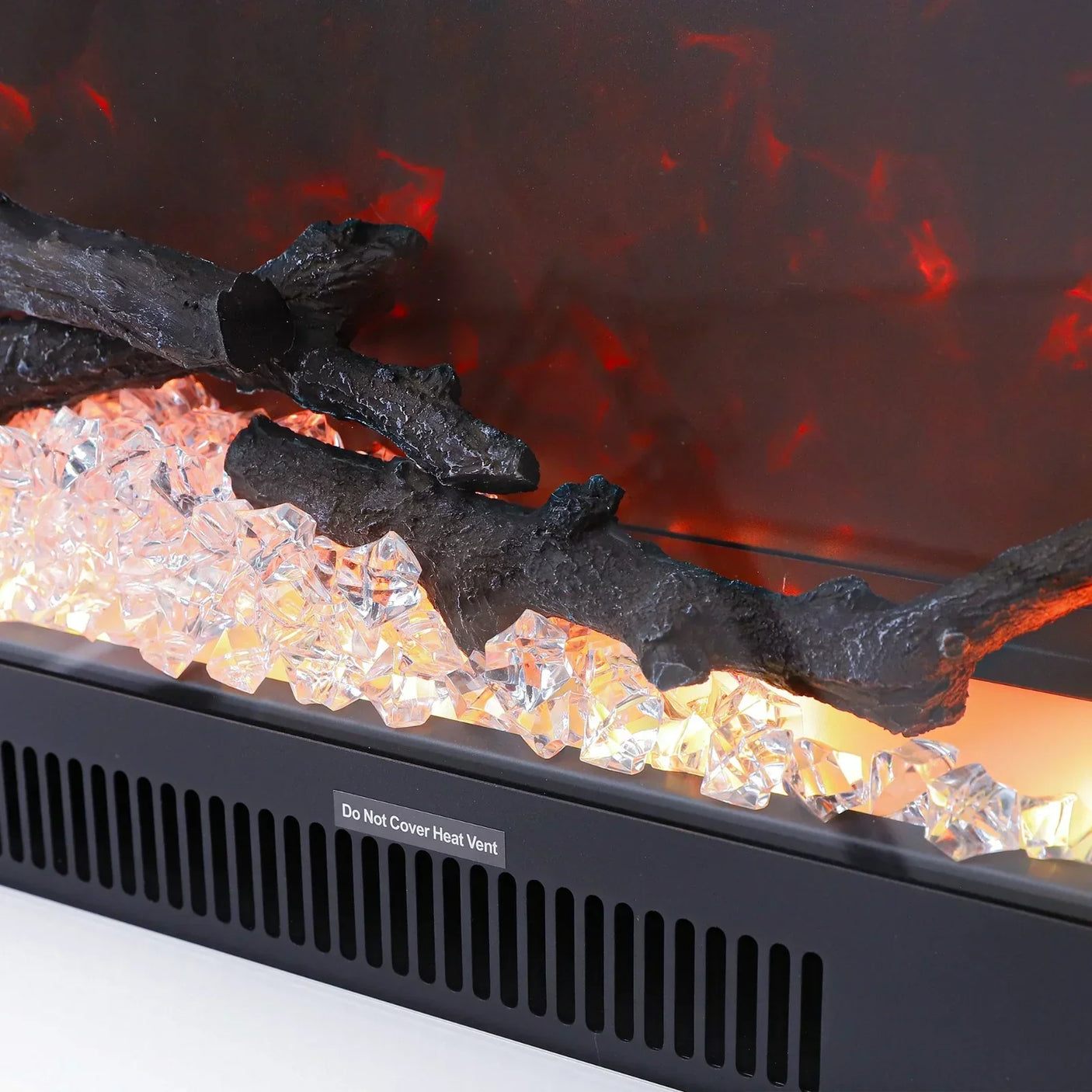 Electric fireplace close-up with faux logs and glass crystals above black heater vent