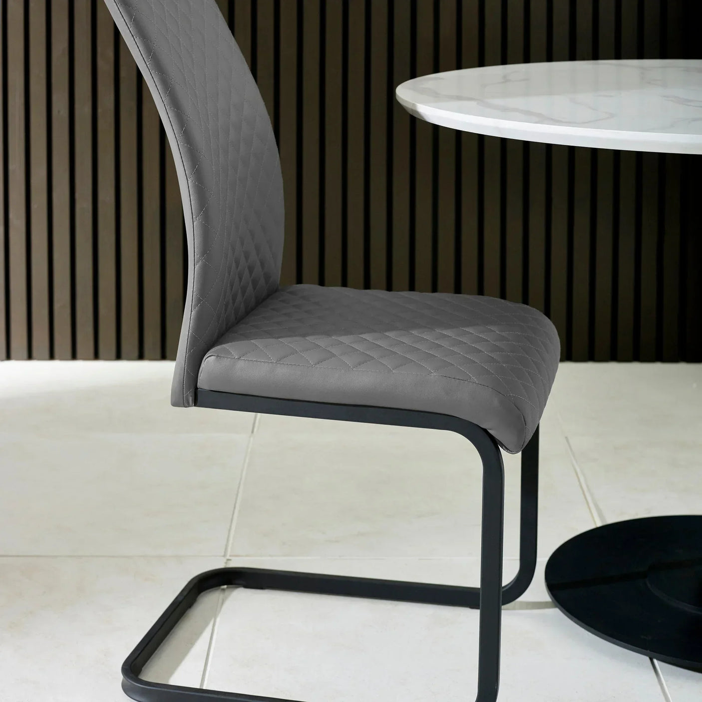 Grey dining chair with quilted seat and black metal frame beside round marble table