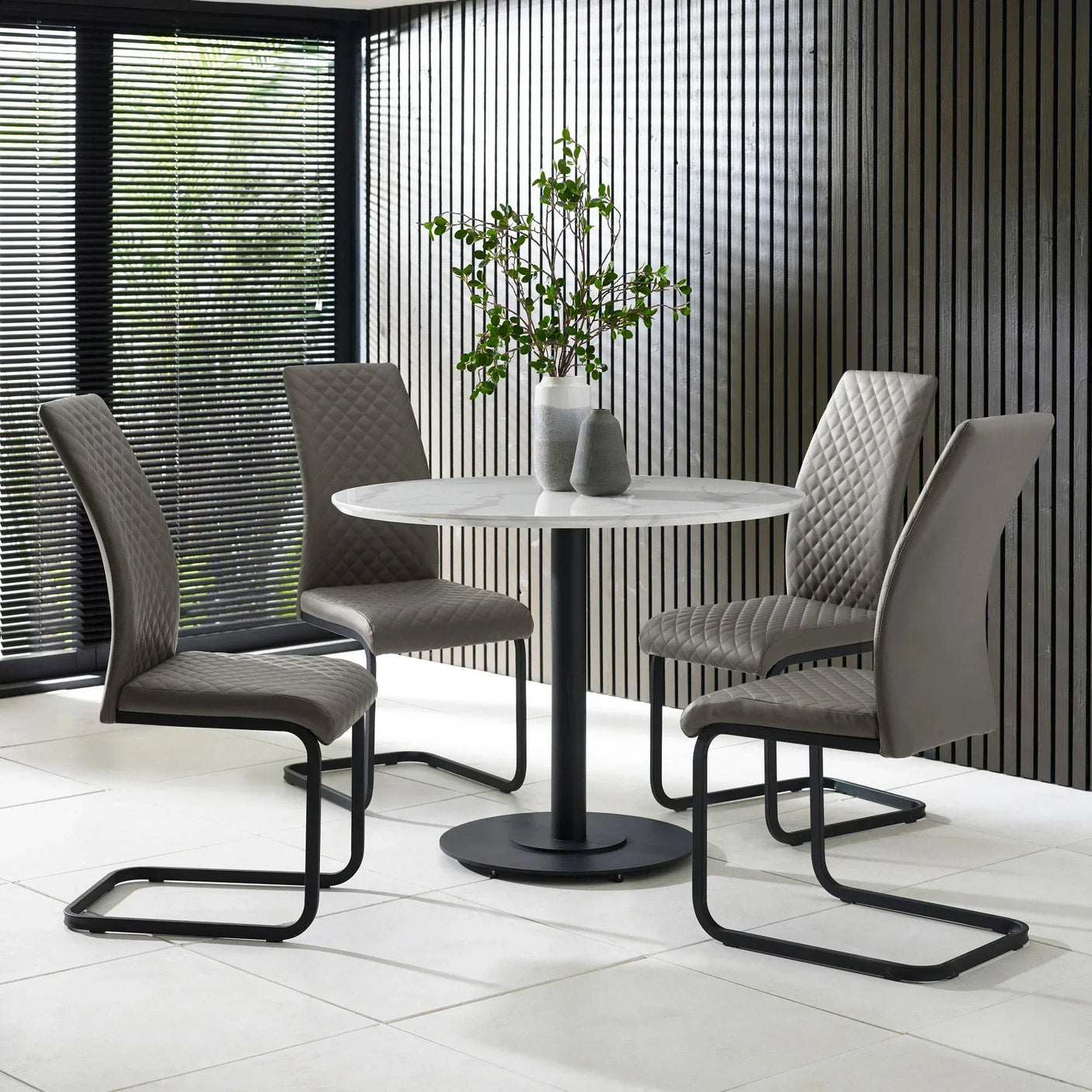 Grey quilted dining chairs with black legs around round white table in modern dining room