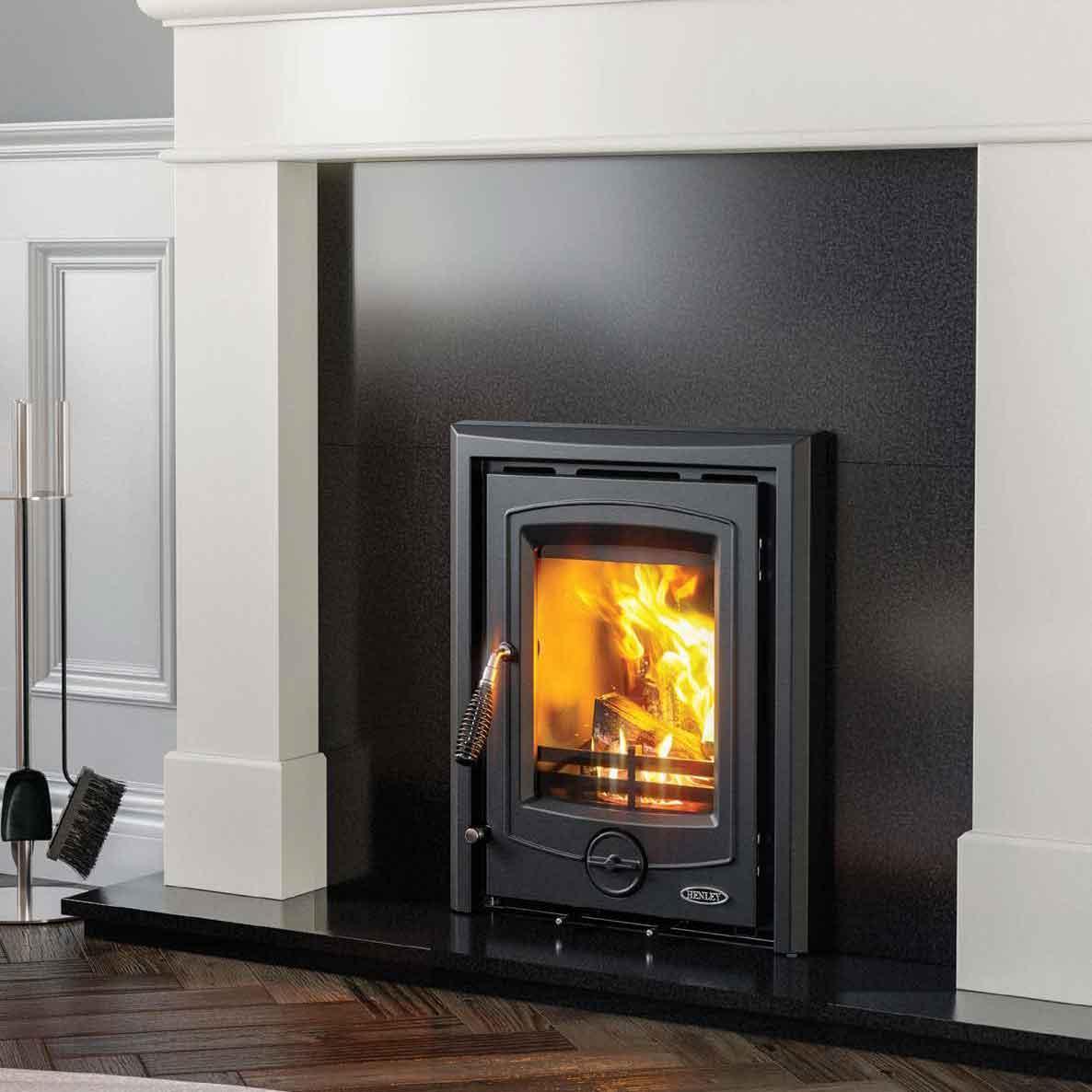 Black wood burning stove with glass door set in modern fireplace, burning logs visible