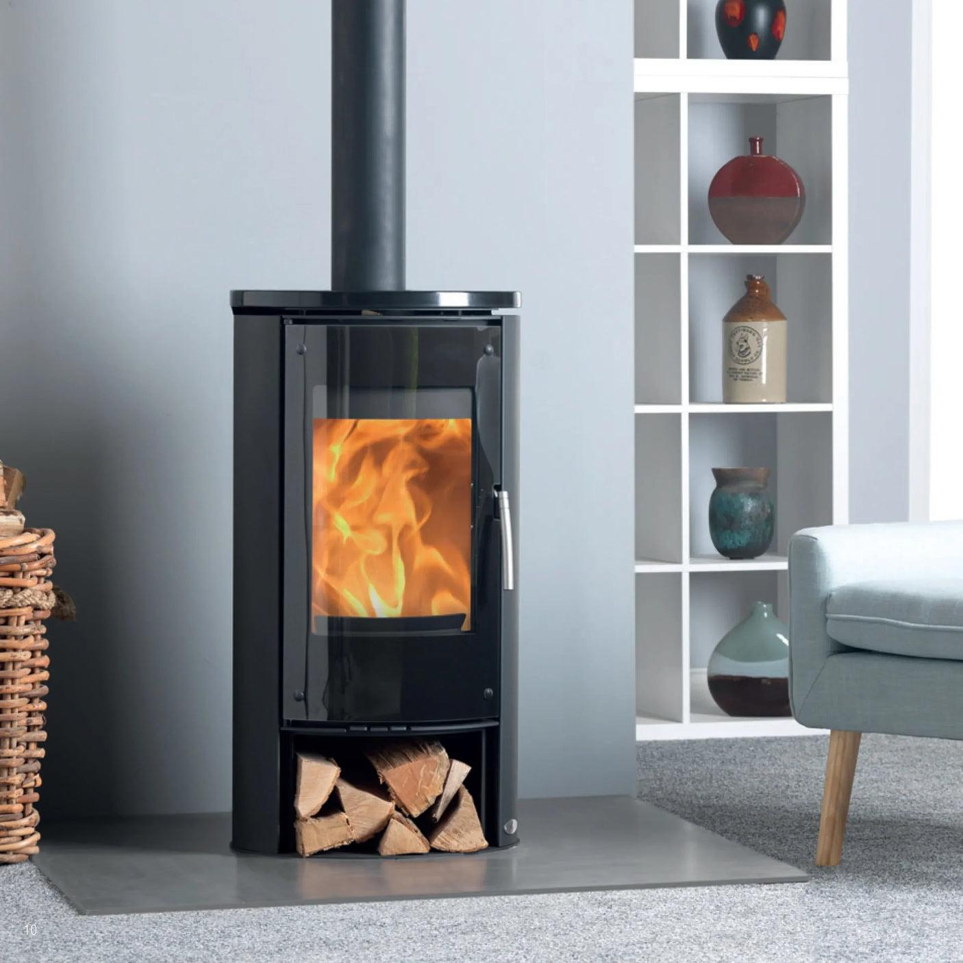 Black wood burning stove with fire, logs below, beside modern shelving and grey armchair