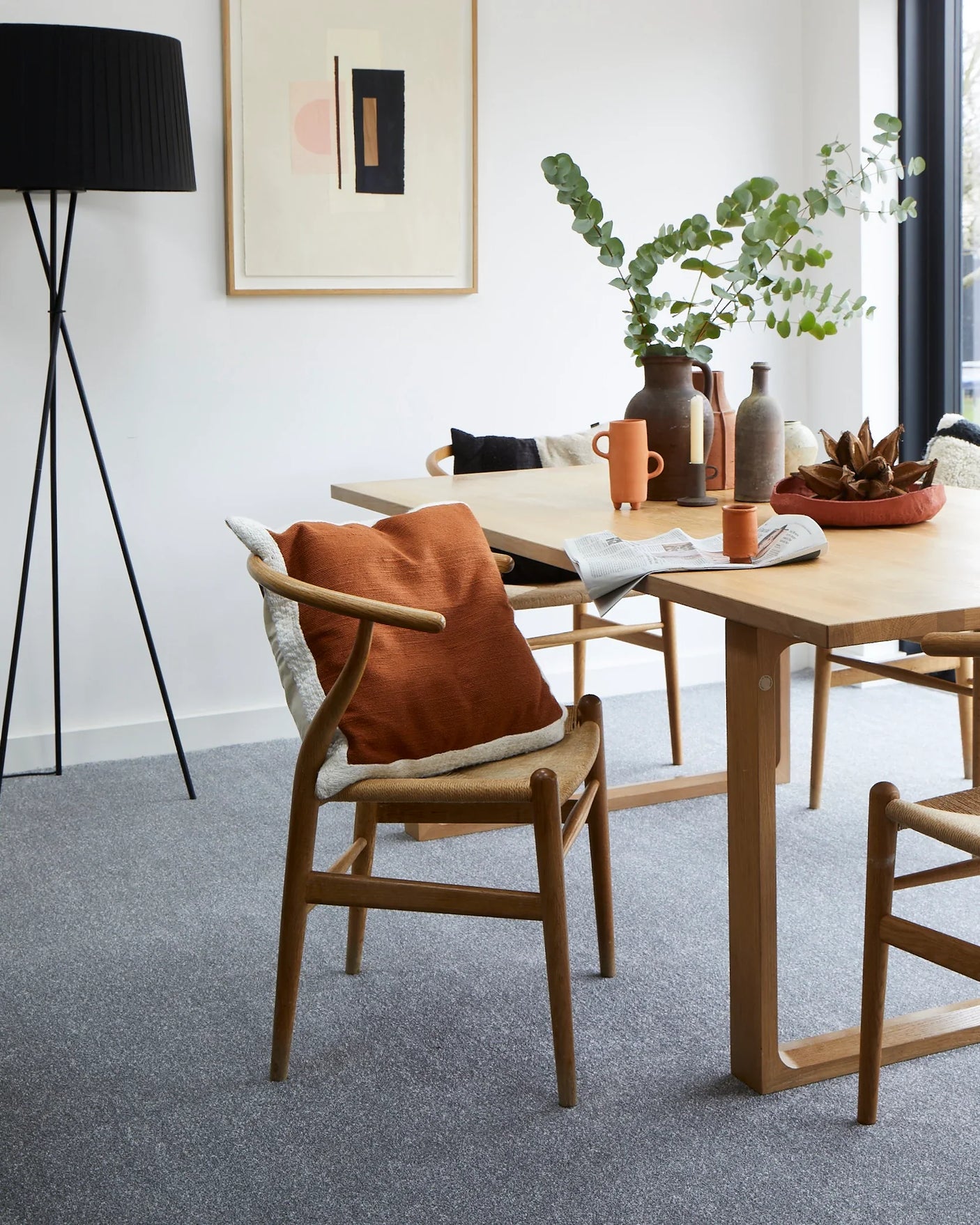 Oak dining table with modern wooden chairs, burnt orange cushion, ceramic vases and greenery