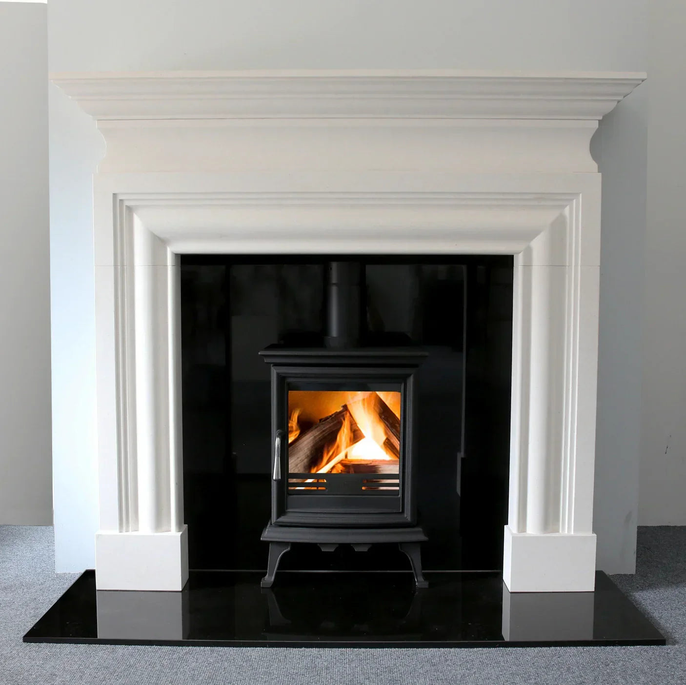 Modern white fireplace surround with black wood burner and glass front on black hearth