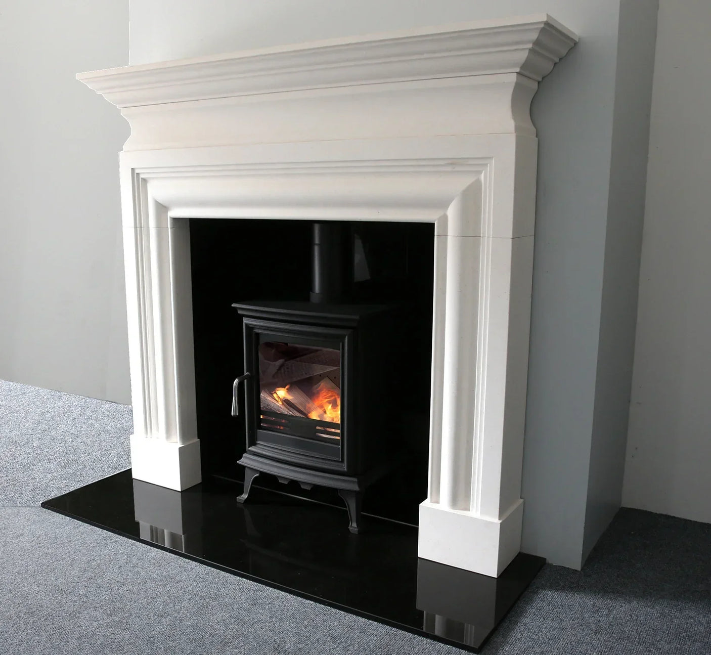 White stone fireplace surround with black wood burning stove and black hearth
