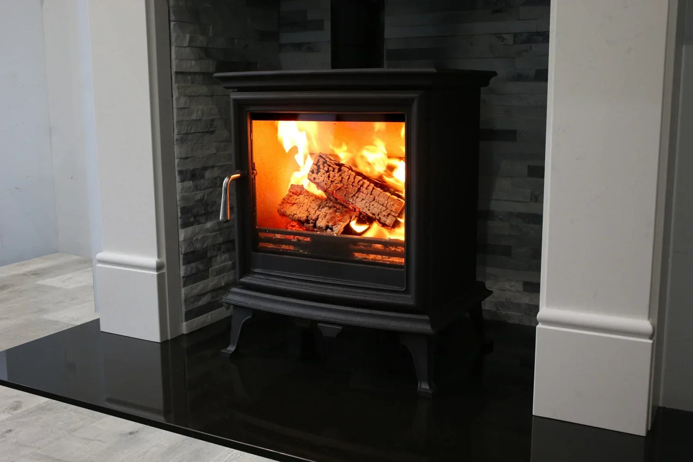 Black wood burning stove with logs and flames set against stone fireplace