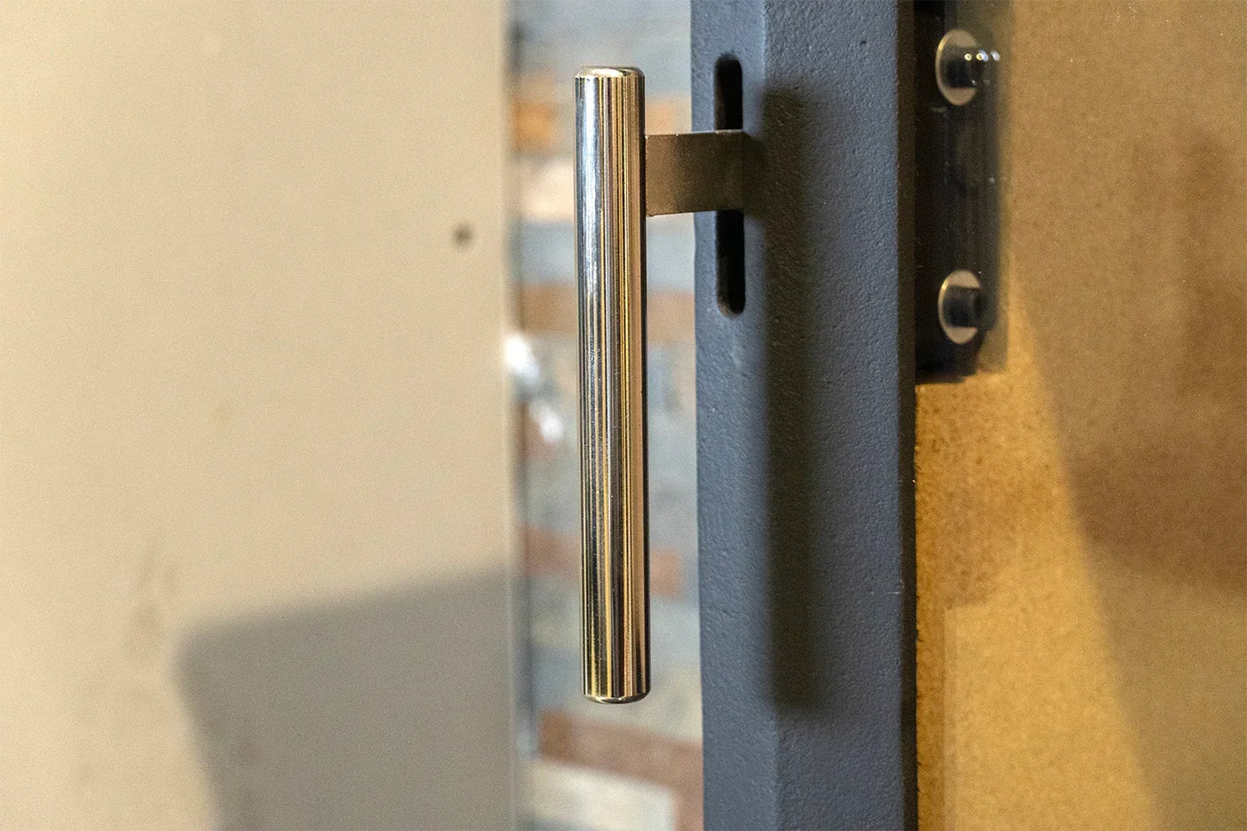 Stainless steel door handle mounted on a black metal frame with wood and glass detail