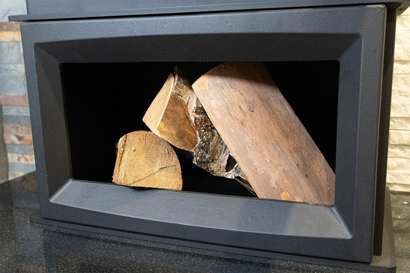 Black log storage box with stacked firewood on a stone surface