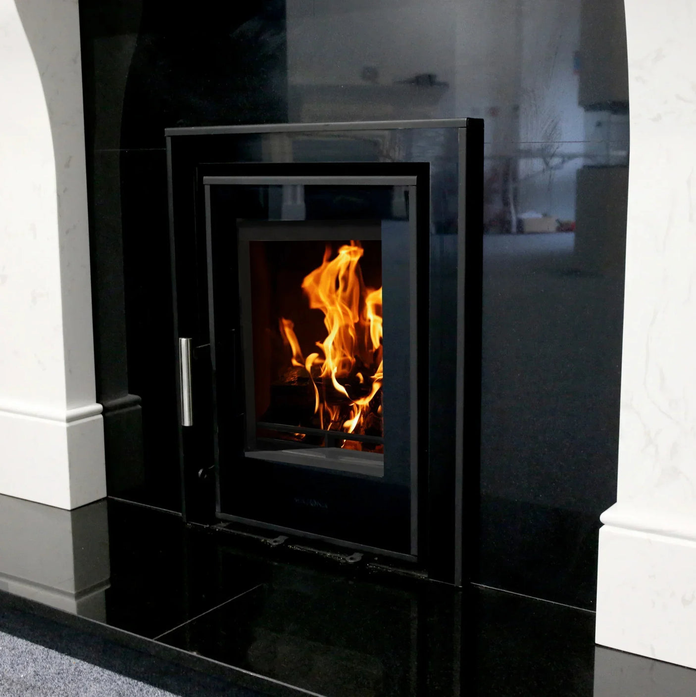 Black glass front wood burning stove installed in marble fireplace surround