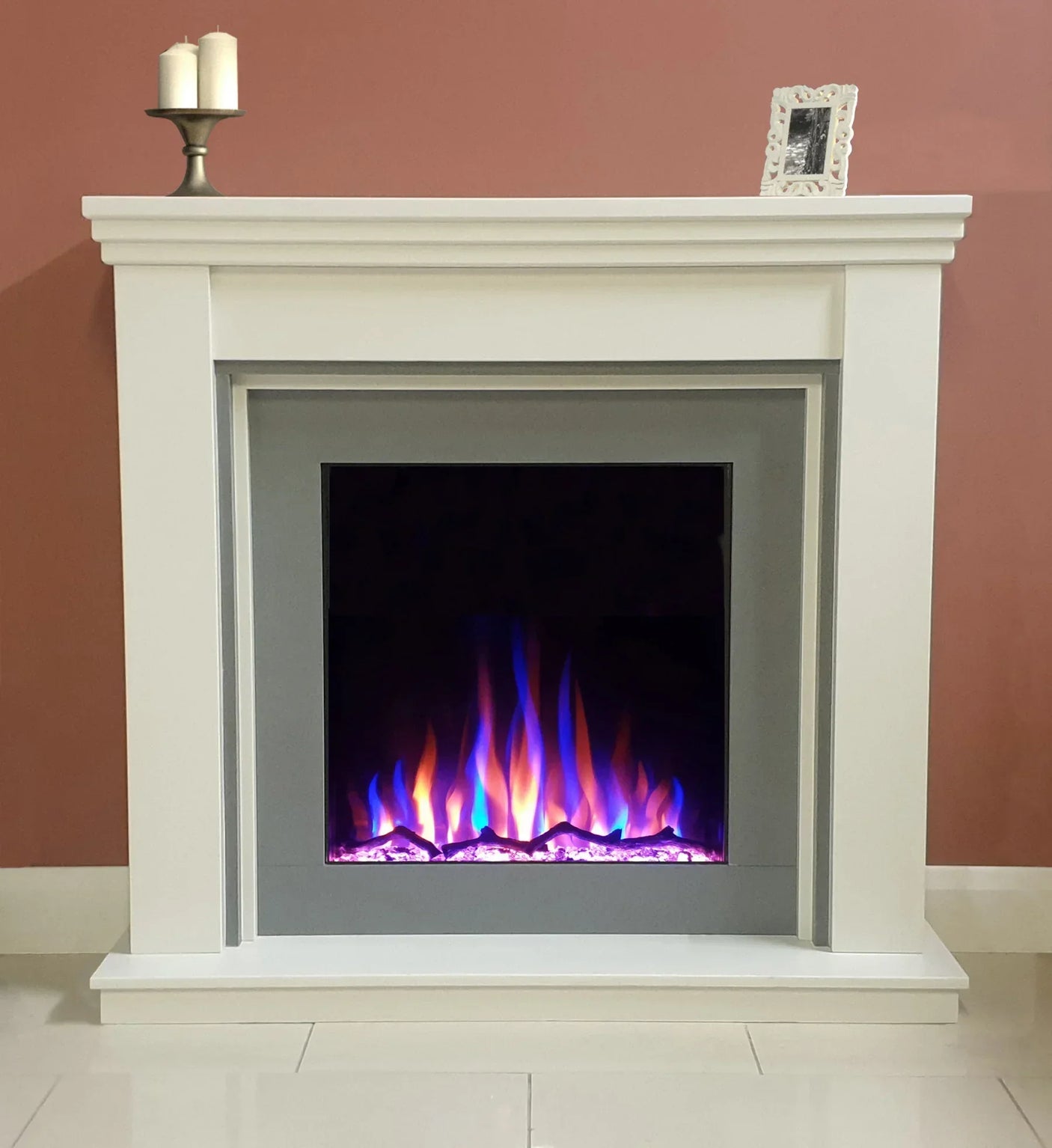 White electric fireplace with glowing multicolour flames and candles on mantel