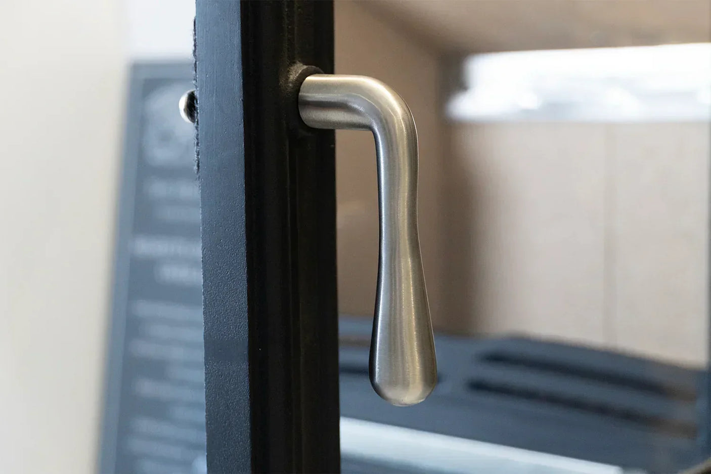 Brushed steel door handle attached to a black metal frame, close-up view