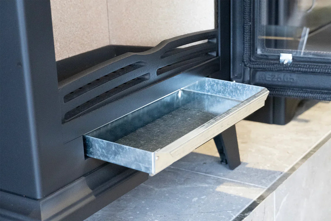 Steel elmwood tray fitted into black stove ash drawer on stone hearth