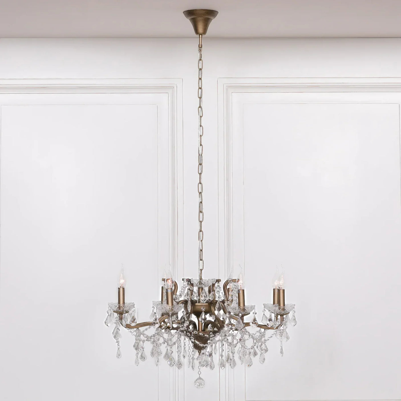 Brass crystal chandelier with candle-style lights and hanging glass droplets in white room