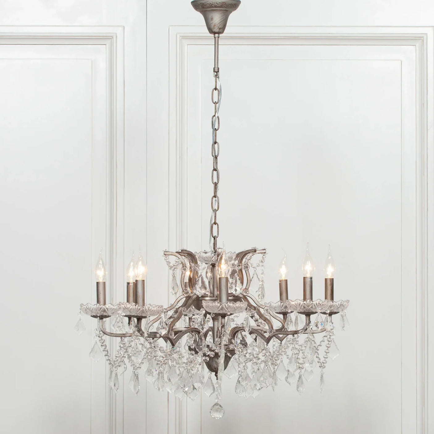 Crystal chandelier with eight candle-style lights and hanging glass prisms against white wall