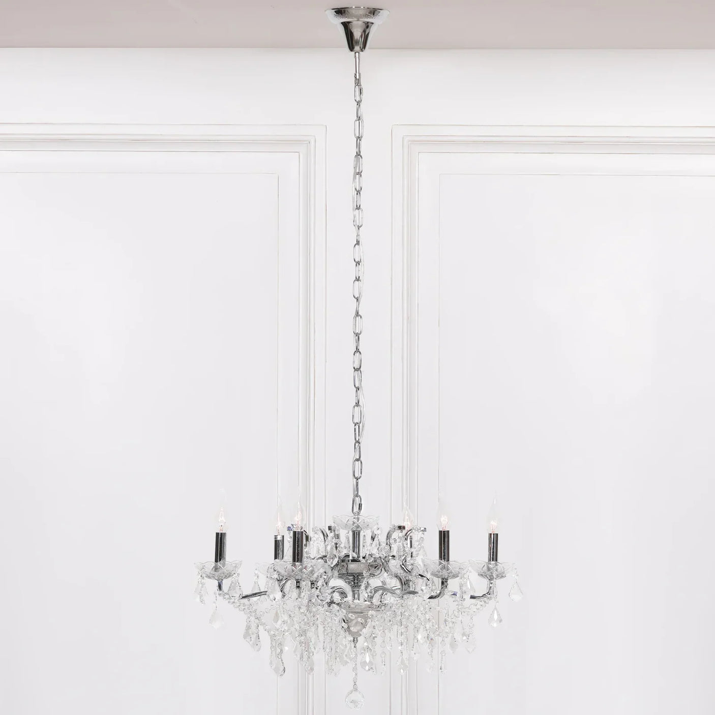 Crystal chandelier lighting with six candle bulbs and chrome chain hanging in white room