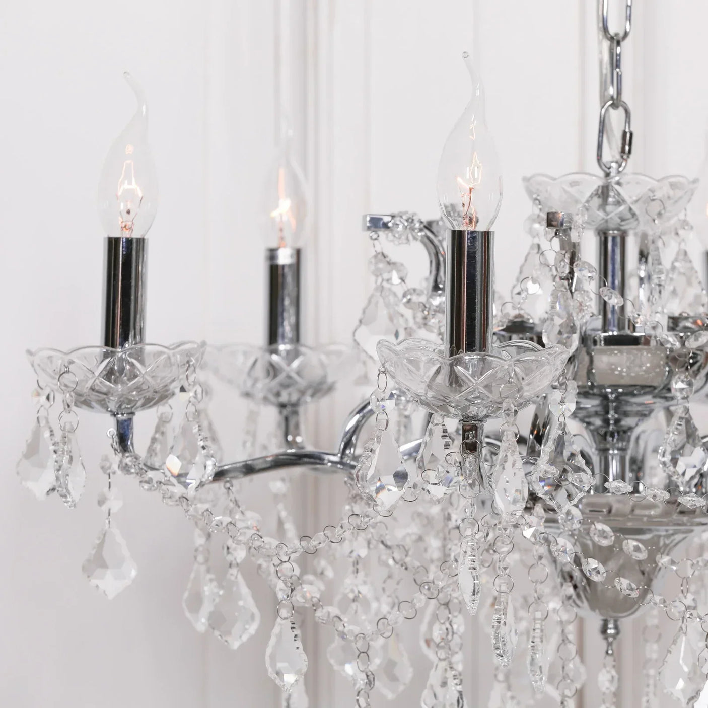 Crystal chandelier with chrome arms and candle-style bulbs, detailed hanging glass droplets