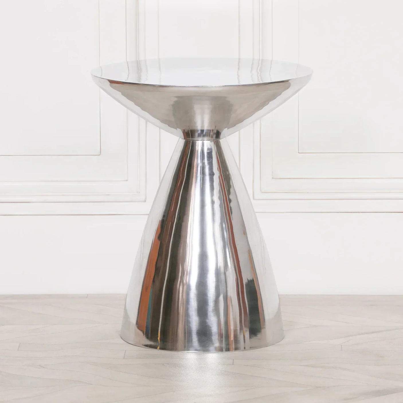 Polished metal side table with hourglass base and round top in modern interior setting