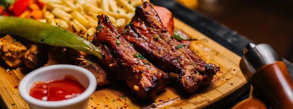 Grilled pork ribs with fries, roasted vegetables, and dip on a wooden serving board