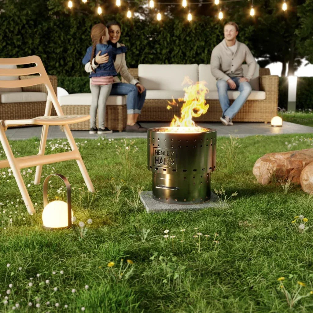 Stainless steel garden fire pit burning on lawn with rattan outdoor sofa and string lights