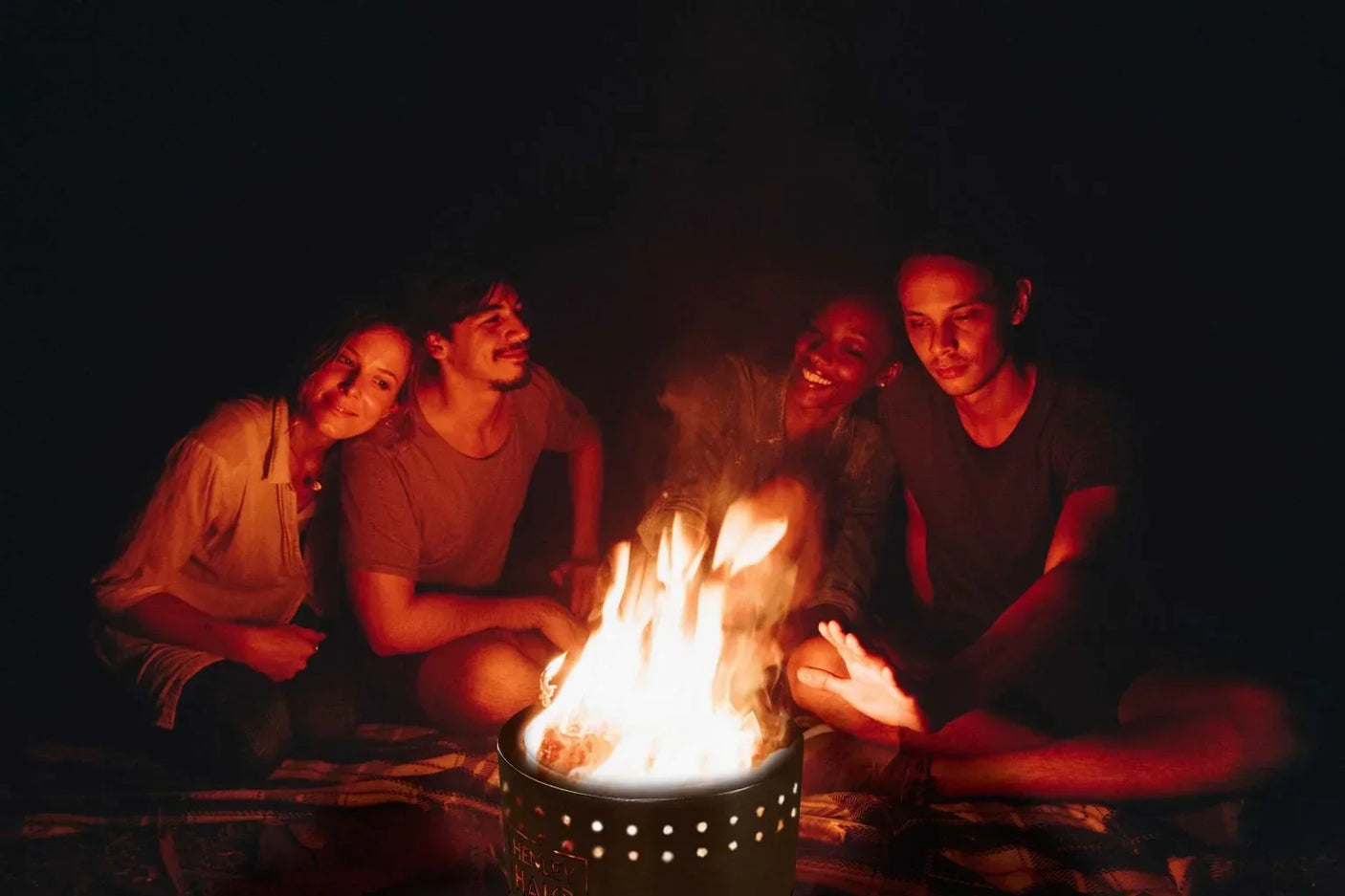 Outdoor fire pit in use at night with four people gathered around, warming by the flames