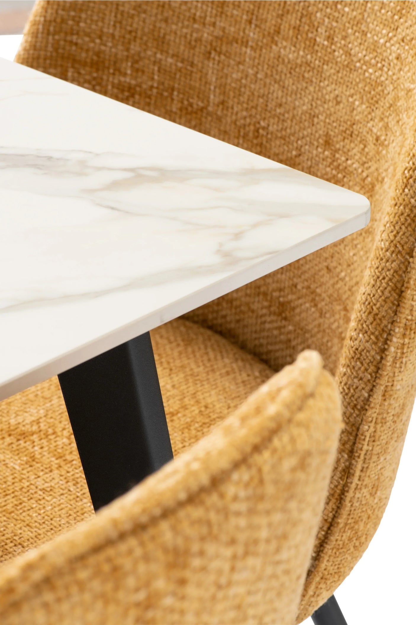 Close view of marble dining table corner with black leg beside textured mustard chair