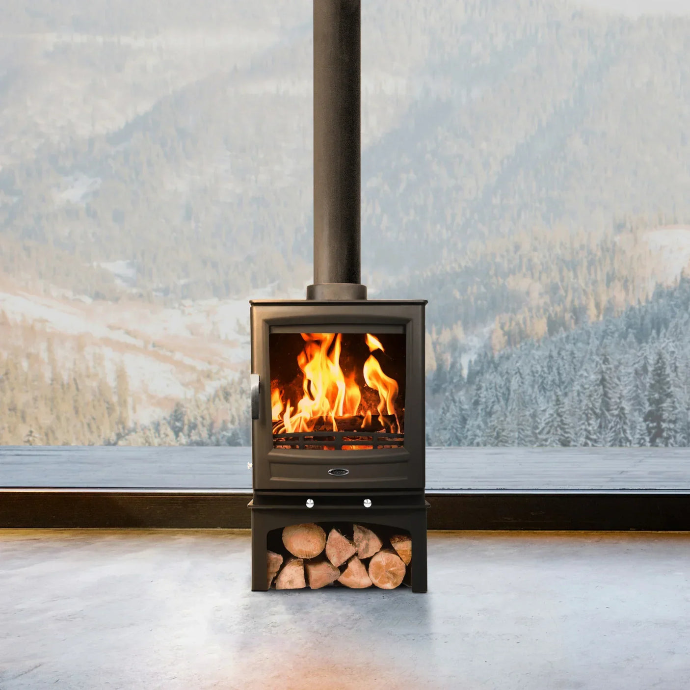 Black wood burning stove with visible fire and log storage against snowy mountain window view