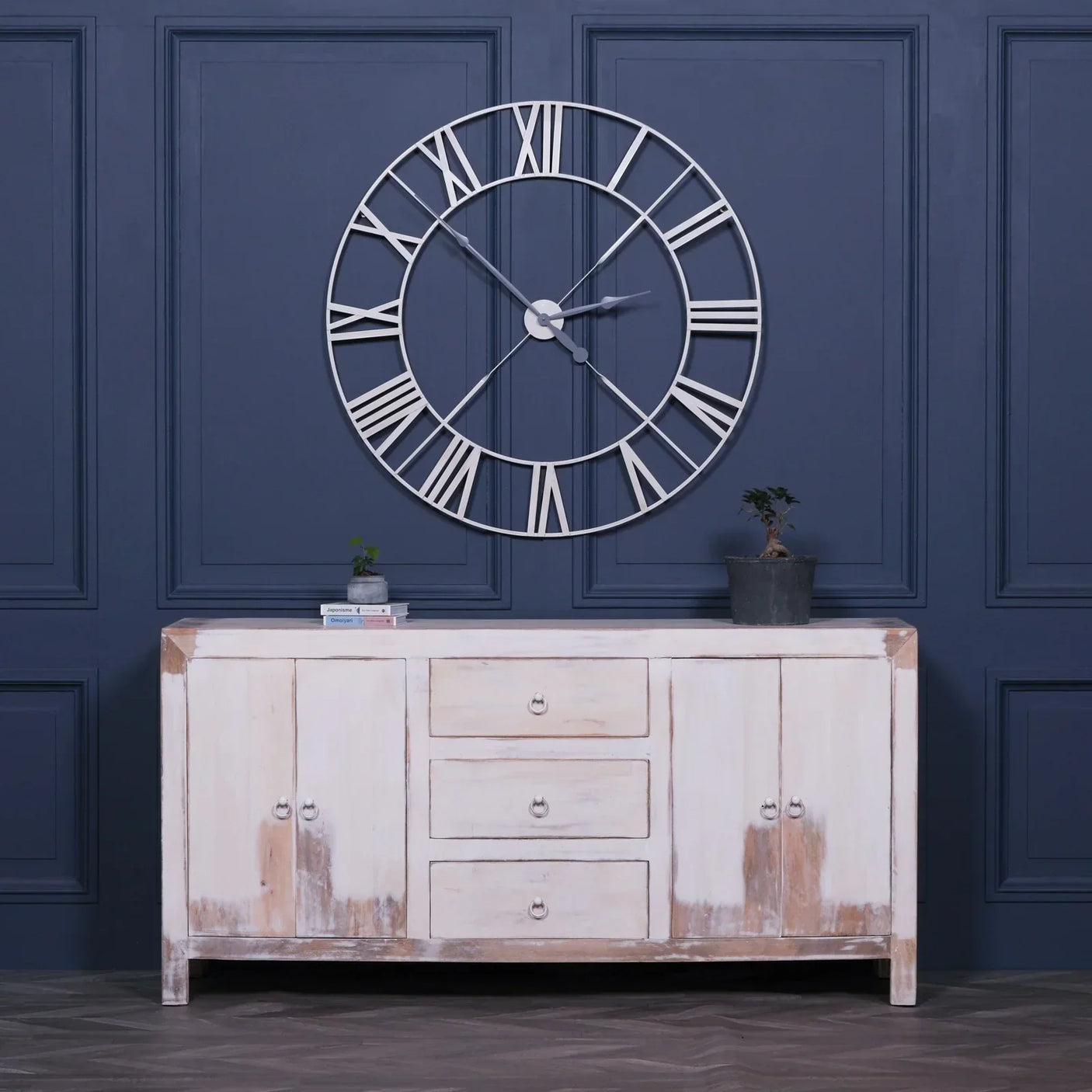 Large open frame wall clock with Roman numerals above distressed wooden sideboard in modern room