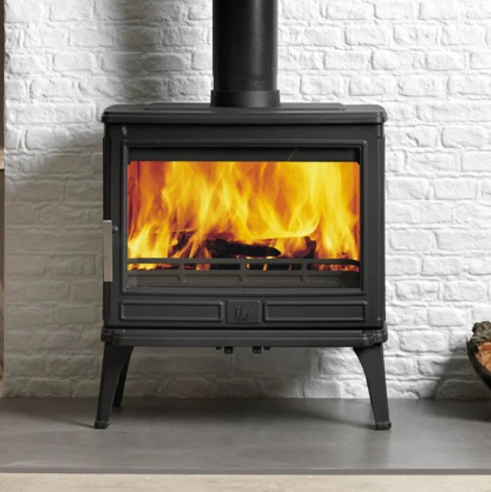 Black cast iron wood burning stove with fire in front of white brick wall