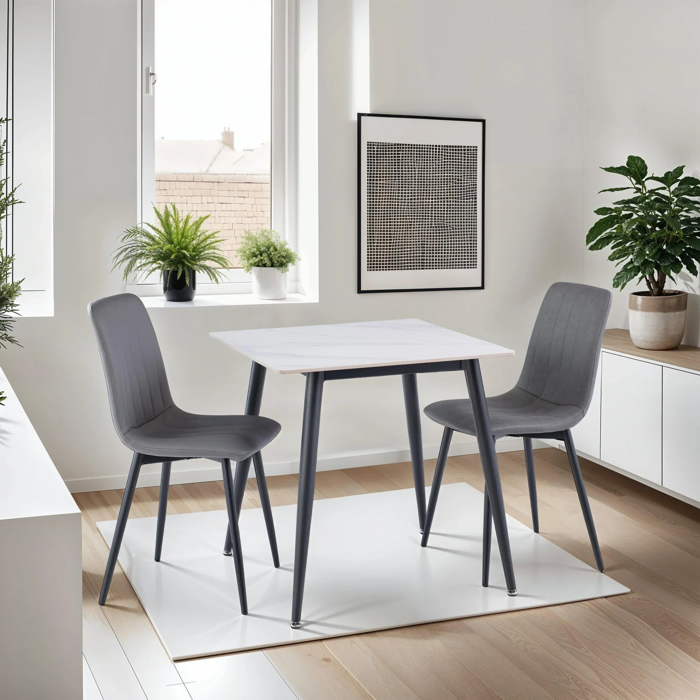 Grey dining table set with two chairs in modern kitchen space with plants and wall art
