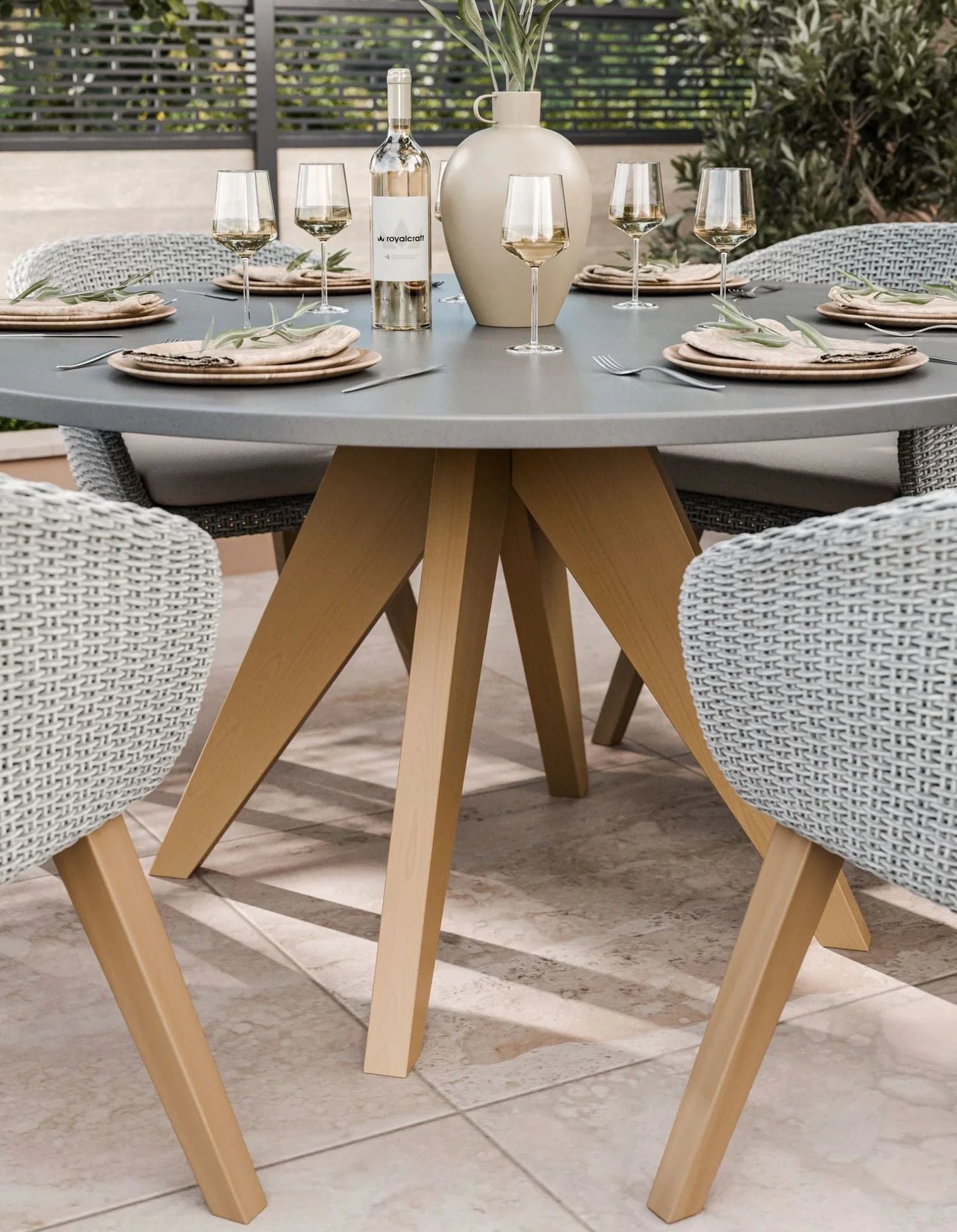 Round grey outdoor dining table with wooden legs and rattan chairs set for four