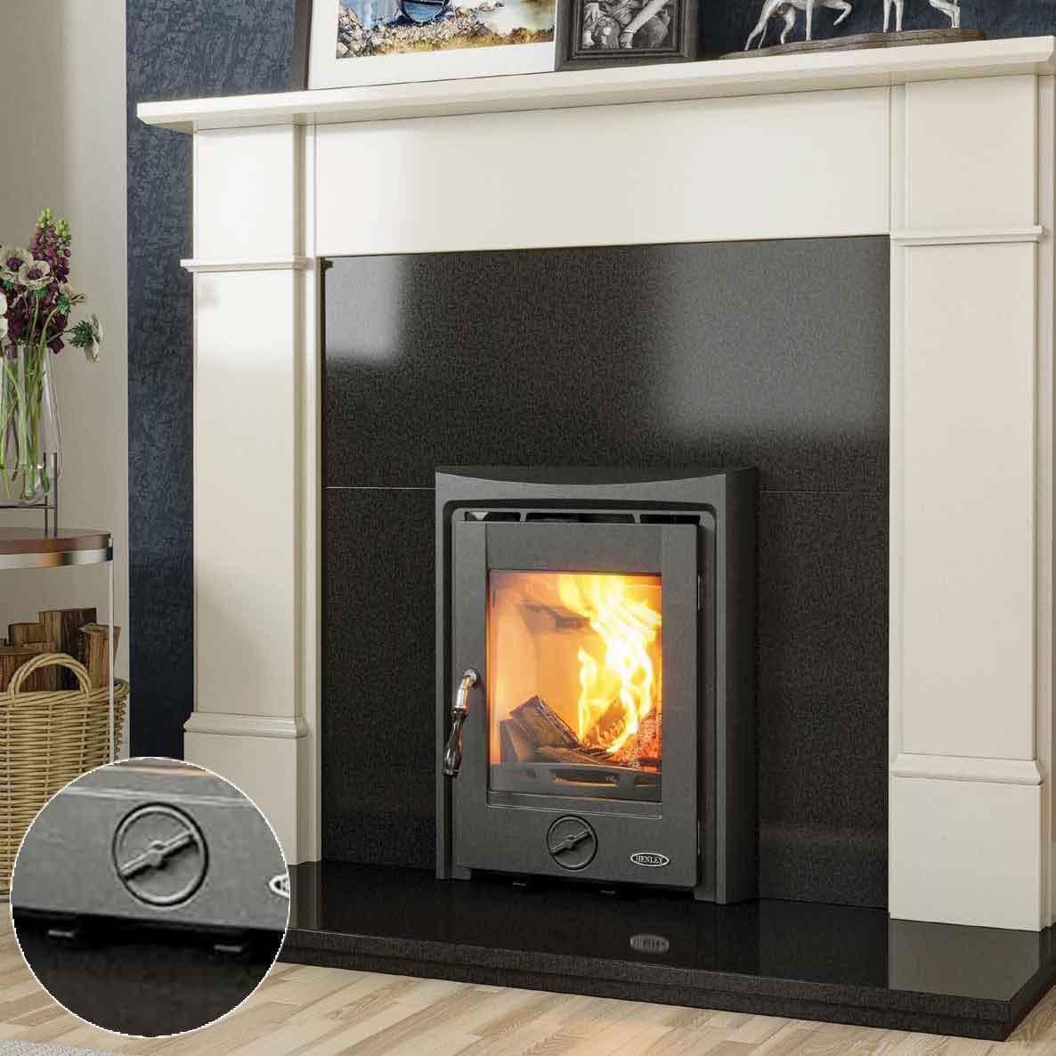 Black wood burning stove with glass door set in modern fireplace, firewood basket nearby