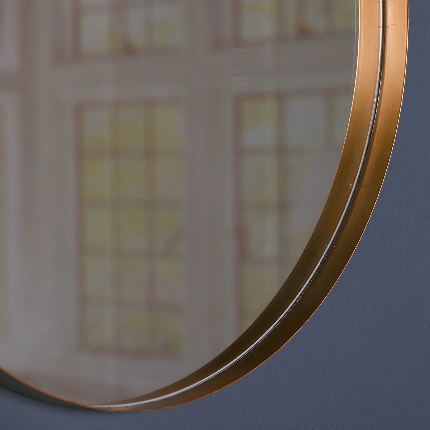 Closeup of round wall mirror with gold metal frame against blue wall