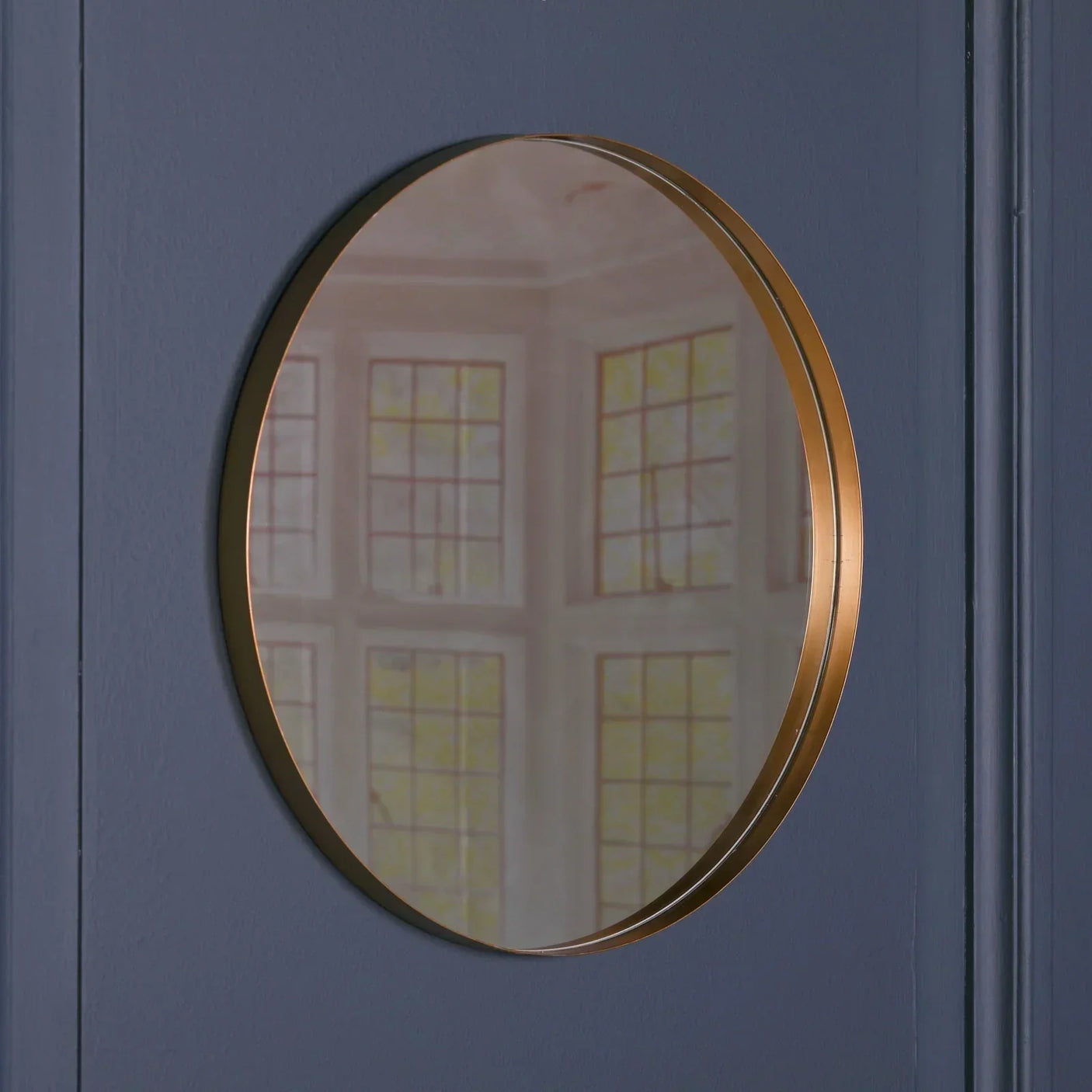 Round wall mirror with gold metal frame mounted on blue panelled wall