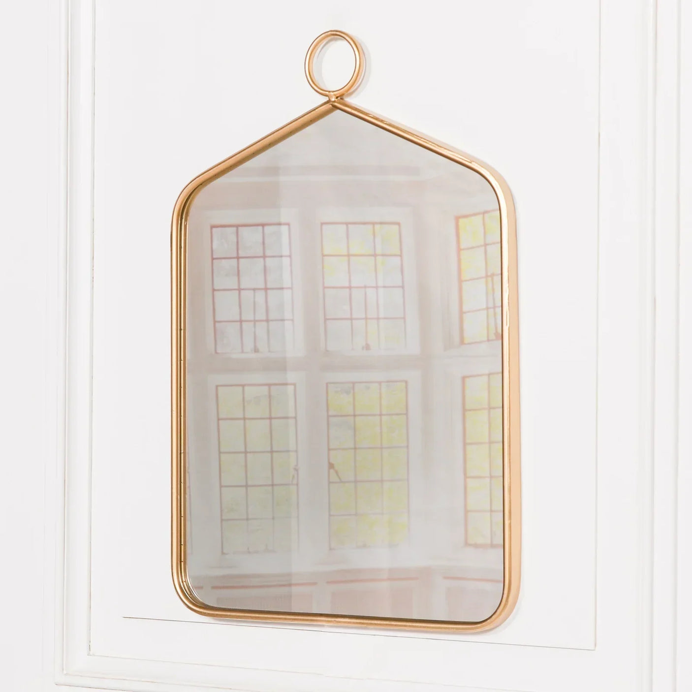Gold metal framed wall mirror with hanging loop on white wall