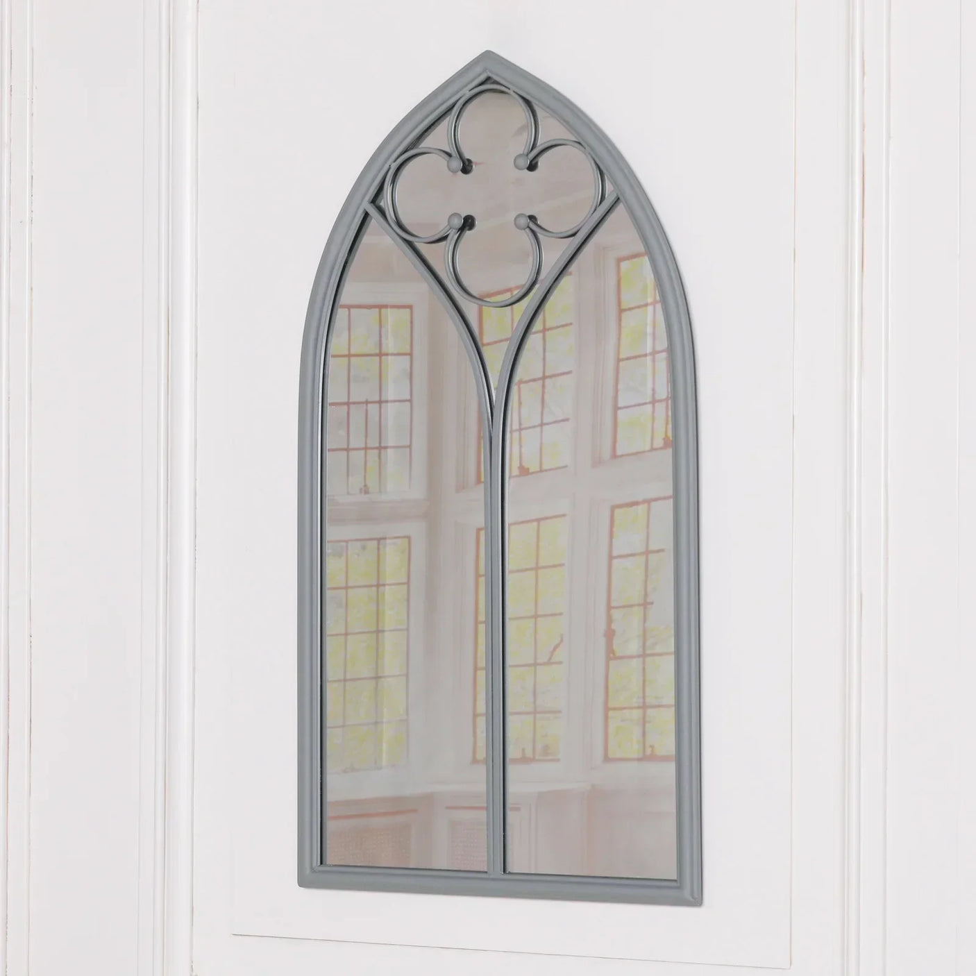 arched wall mirror with grey metal frame and quatrefoil detail mounted on white panel wall