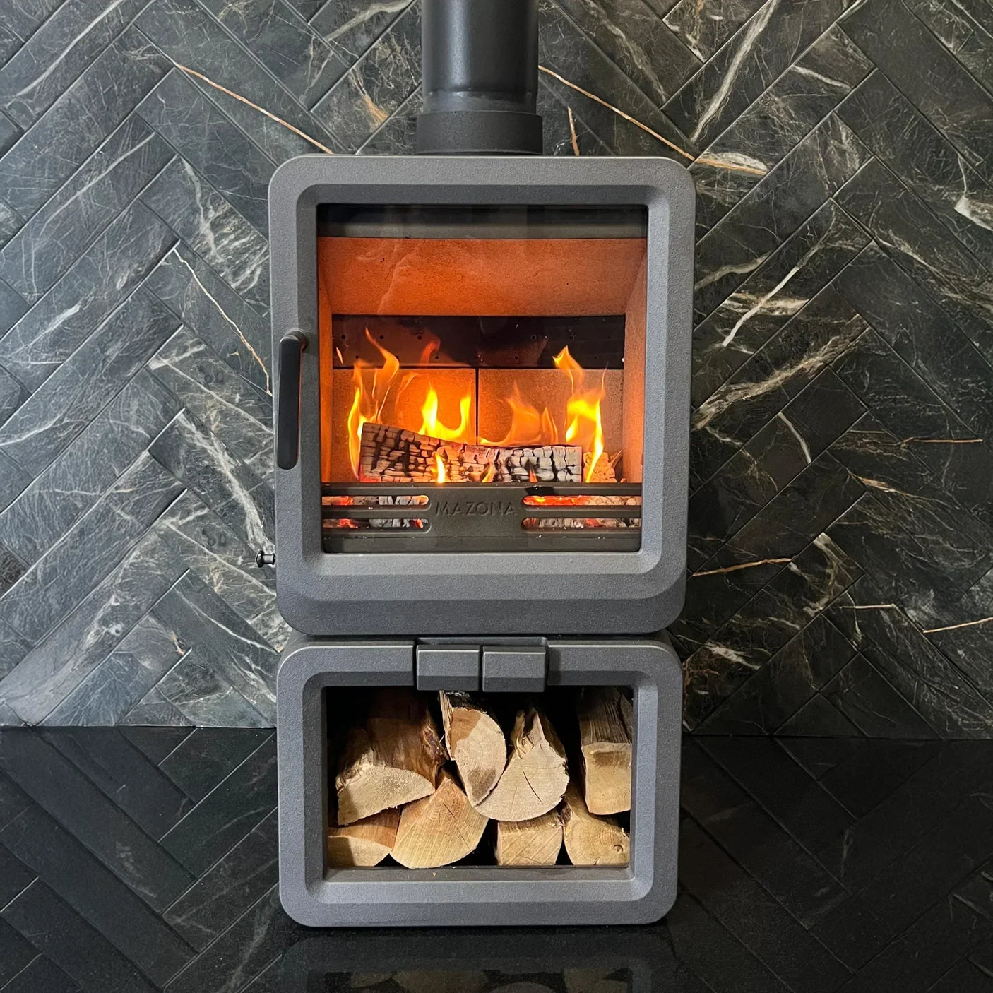 Modern wood burning stove with glass door and log storage against black tile wall