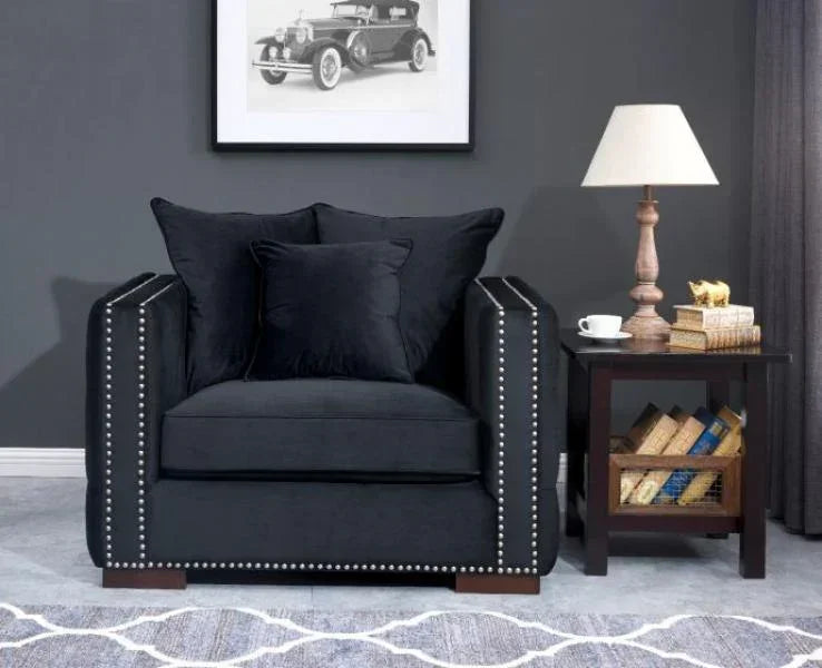 Black velvet armchair with silver studded trim next to dark wooden side table and lamp