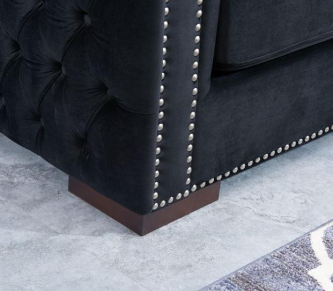 Corner of black velvet sofa with button tufting and studded trim on wooden leg