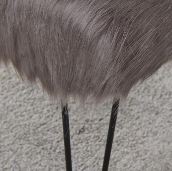 Grey faux fur stool with black metal legs on textured carpet