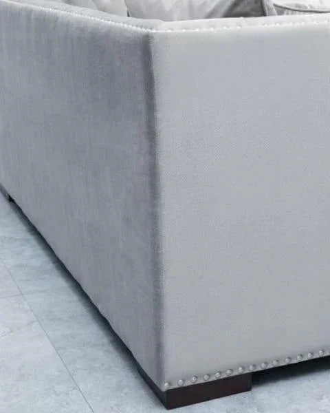 Closeup of light grey fabric sofa corner with stud detailing and dark wooden leg