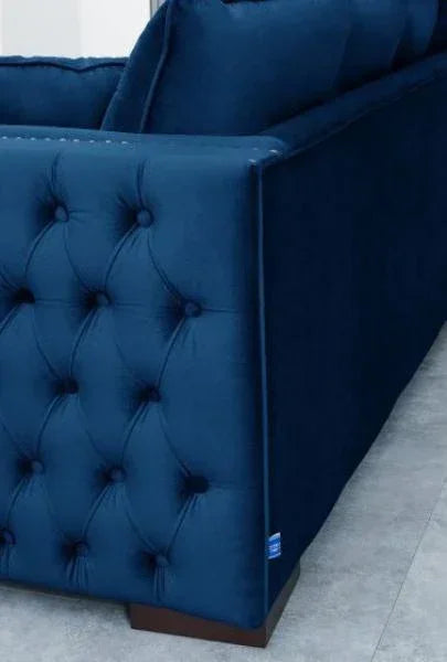 Navy blue velvet sofa with tufted side detail and dark wooden legs on tiled floor