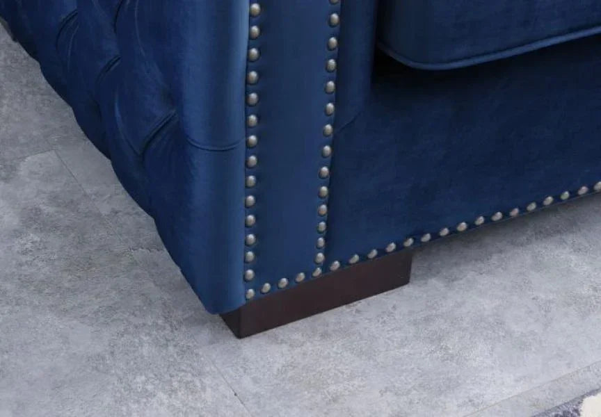 Blue velvet sofa with silver nailhead trim and dark wooden leg on tiled floor